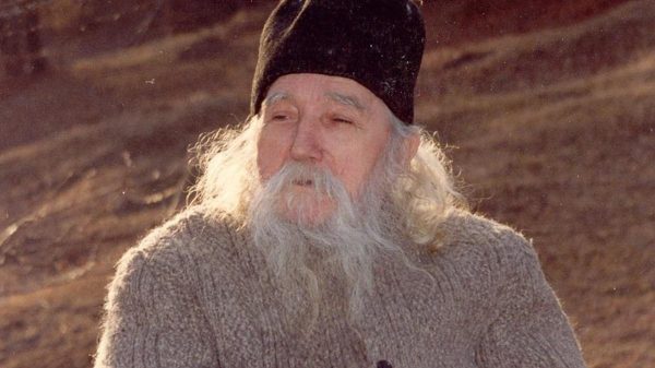 Un preot batran cu caciula pe cap care se afla pe camp.