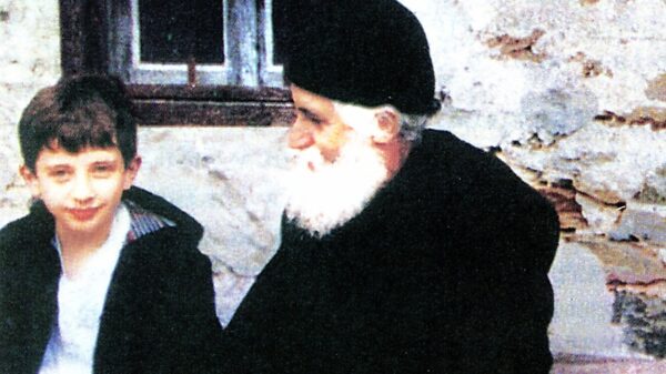 Un calugar batran sta pe o banca langa u copil.