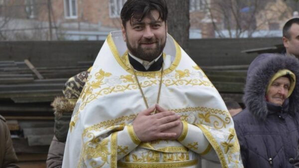 Un preot ortodox imbracat in vesminte de slujba si mai multi credinciosi in curtea parohiei.